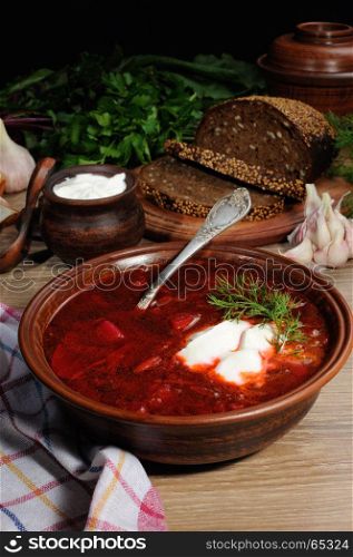 Borscht-vegetable beetroot soup, on the table with slices of rye cereal bread and gluten of sour cream, garlic and herbs. Rustic style.