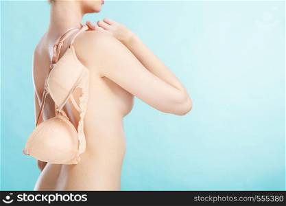 Bosom concept. Slim attractive naked woman holding beige plunge bra in hand, on blue. Naked woman holds beige bra in hand