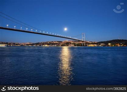 Bosphorus Bridge on the background of the night coast under the bright moon. Istanbul, Turkey. Night landscape.. Bosphorus Bridge on background of night coast under bright moon