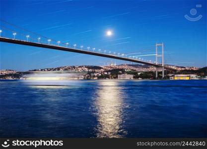 Bosphorus Bridge under the night sky with moon and star tracks. Istanbul, Turkey. Bosphorus Bridge with track of the ship