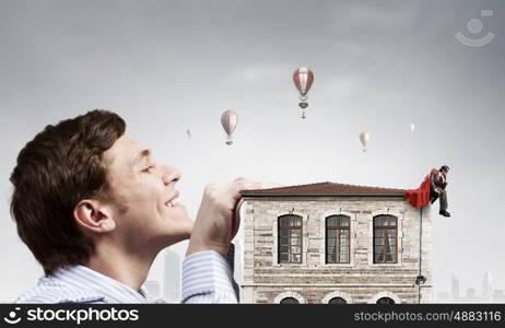 Boss peeping from under table. Bored businessman with red cape sitting on the roof of building