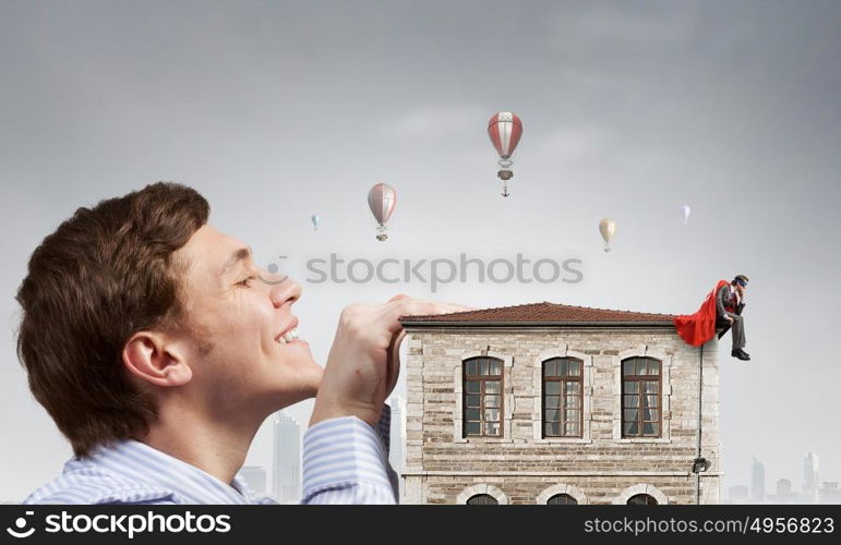 Boss peeping from under table. Bored businessman with red cape sitting on the roof of building