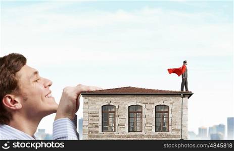 Boss peeping from under table. Businessman with red cape staying on the roof of building