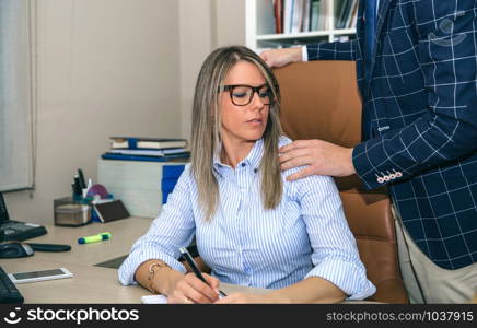 Boss putting hand over shoulder of blonde secretary in the office. Sexual harassment at work concept.. Boss sexual harassing to blonde secretary at workplace