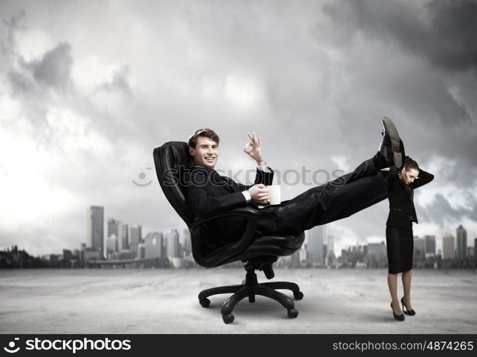 Bossy businessman. Young businessman sitting gin chair with legs on colleagues shoulders