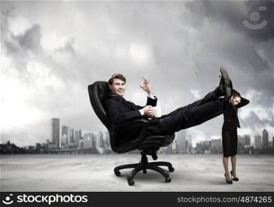 Bossy businessman. Young businessman sitting gin chair with legs on colleagues shoulders
