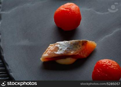 Bota sardine slice with osmotized tomatoes macro closeup on black slate dish