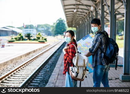 Both male and female tourists look at the map beside the railway.