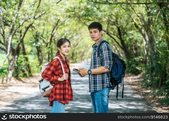 Both male and female tourists stand to see the map on the road.