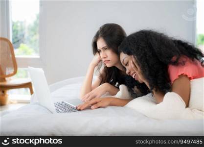 Both of  young women use laptops to browse information and contact friends online in bedroom of the house. LGBT concept.