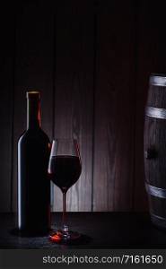 Bottle and a glass of red wine against the background of barrels and boards. Bottle and glass of red wine against background of barrels and boards