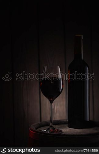 Bottle and a glass of red wine stand on an old wooden barrel. Wooden background.. Bottle and glass of red wine stand on old wooden barrel