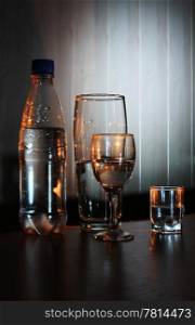 Bottle and a glass of water on a dark background with light