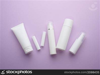 bottle and empty white plastic tubes for cosmetics on a purple background. Packaging for cream, gel, serum, advertising and product promotion, mock up