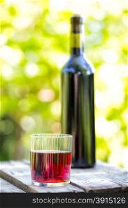 Bottle and faceted glass red wine against blurred background of green foliage. Bottle and faceted glass red wine