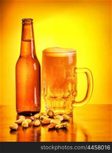 Bottle and glass full of beer with pistachio nuts on the table on yellow background, october beer fest, tasty alcoholic drink &#xA;