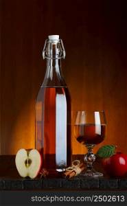 Bottle and glass of apple cider with sliced apple on wooden table with cinnamon and anise star