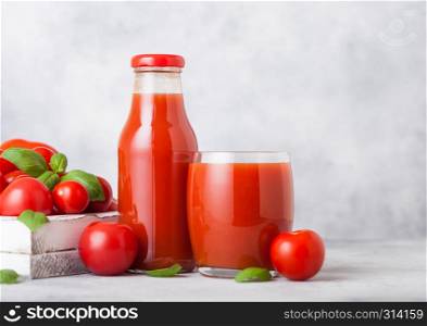 Bottle and glass of fresh organic tomato juice with fresh raw tomatoes in box on kitchen background.