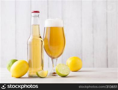 Bottle and glass of lager beer with lemon and lime on light wooden background