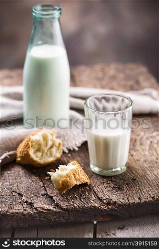 Bottle and glass of milk with slices of bread on a wooden table. Bottle and glass of milk with slices of bread