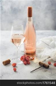 Bottle and glass of pink rose homemade wine with corks, corkscrew and grapes on light table background. Top view