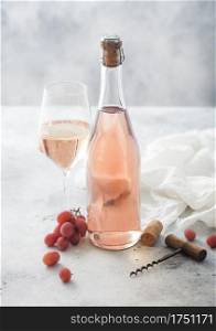Bottle and glass of pink rose homemade wine with grapes and corkscrew with linen cloth on light table background.
