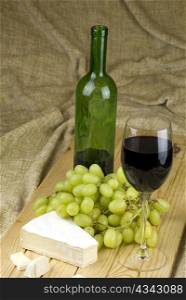 bottle and glass of red white grapes and brie cheese on brown background