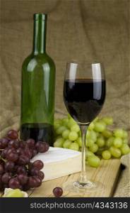 bottle and glass of red white grapes and brie cheese on brown background