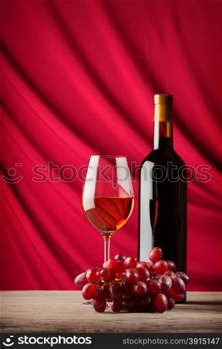 Bottle and glass of red wine on a background of scarlet satin falling waves. Bottle and glass of red wine on a background of scarlet satin