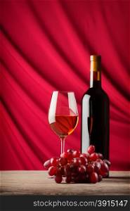 Bottle and glass of red wine on a background of scarlet satin falling waves. Bottle and glass of red wine on a background of scarlet satin
