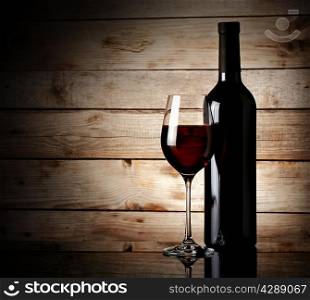 Bottle and glass of red wine on a wooden background