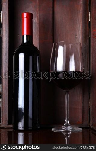 Bottle and glass of red wine with a wooden box in the background