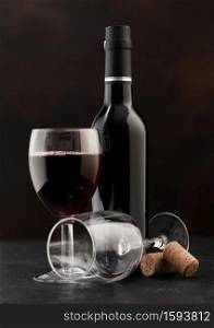 Bottle and glass of red wine with corks on dark background.