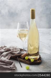 Bottle and glass of white homemade wine with corks, corkscrew and grapes on wooden board with linen cloth on light table background.