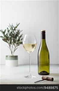 Bottle and glass of white wine and corkscrew on light background.