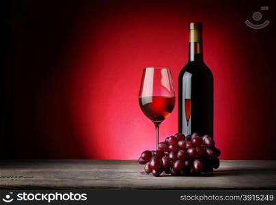 Bottle and glass of wine with grapes on background red velvet. Bottle and glass of wine with grapes