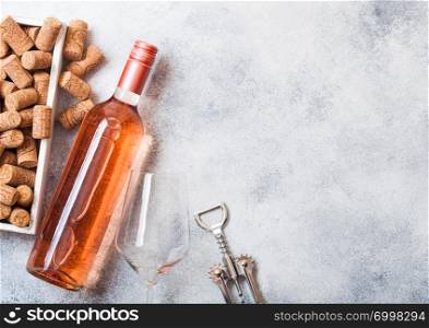 Bottle and glasses of pink rose wine with box of corks and corkscrew opener on stone kitchen table background. Top view.