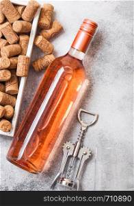 Bottle and glasses of pink rose wine with box of corks and corkscrew opener on stone kitchen table background.