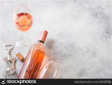 Bottle and glasses of pink rose wine with cork and corkscrew opener on stone kitchen table background. Top view.