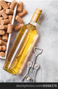 Bottle and glasses of white wine with box of corks and crkscrew opener on stone kitchen table background. Top view.