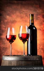 Bottle and two glasses of red wine on wooden barrel with red background. Bottle and two glasses of red wine on wooden barrel