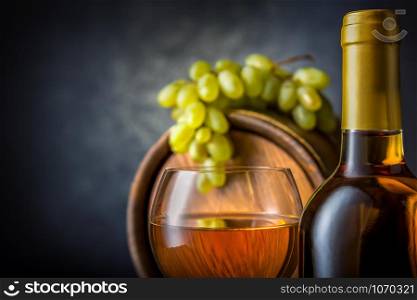 Bottle and wineglass of white wine near barrel in cellar. White wine in cellar