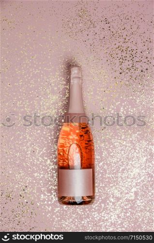 Bottle of champagne with gold glitter on pink background, top view. Hilarious celebration