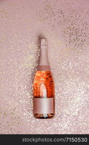 Bottle of champagne with gold glitter on pink background, top view. Hilarious celebration