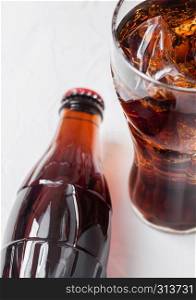 Bottle of cola soda drink and glass with ice cubes next to opener on black stone.