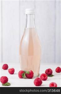 Bottle of cold raspberry soda drink with raw berries on light wooden background