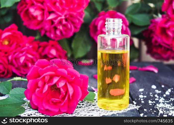 Bottle of fragrant oil with red roses on a wooden table. Aromatherapy.. Bottle of fragrant oil with red roses on a wooden table.