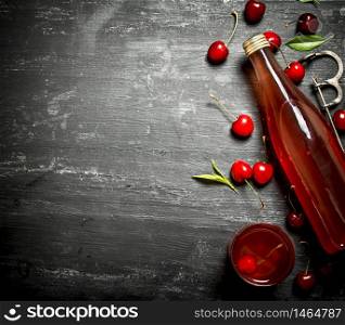 bottle of fresh cherry juice with the leaves around. On a black wooden background.. bottle of fresh cherry juice with the leaves around.