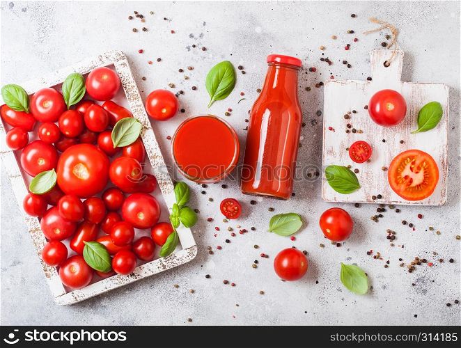 Bottle of fresh organic tomato juice with fresh raw tomatoes basil and pepper in box on stone background