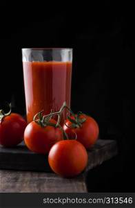 Bottle of fresh organic tomato juice with fresh raw tomatoes in box on kitchen background.